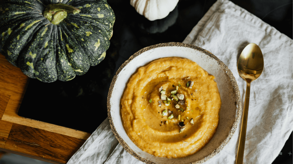 A seasonal squash and soup in a bowl on a tea towel with a spoon. 